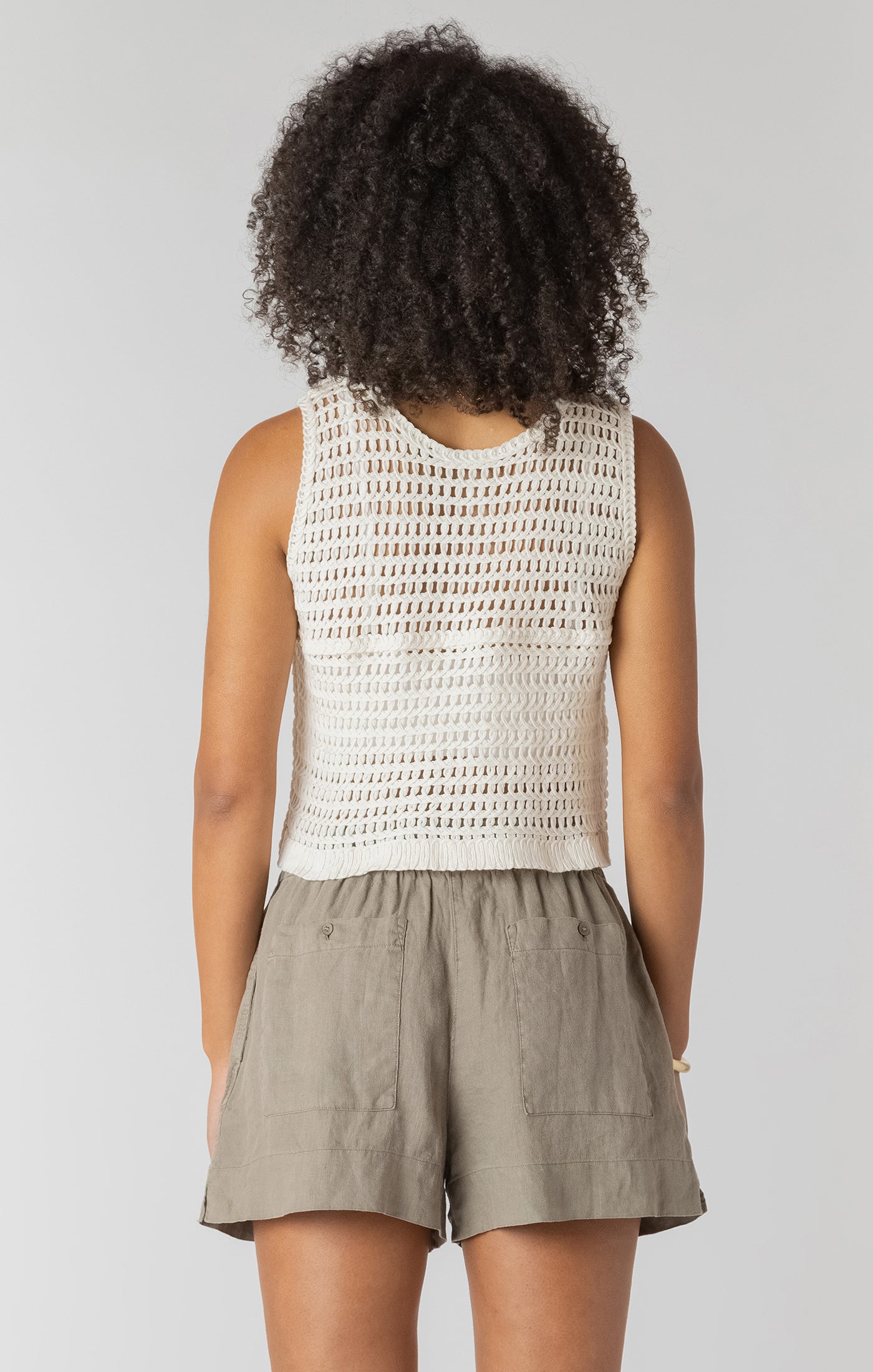 Person wearing a white sleeveless crochet top and beige shorts on a plain background