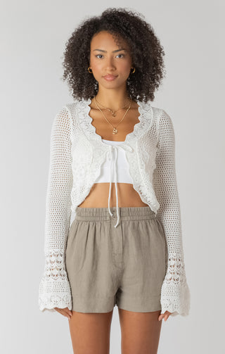 Woman wearing a white crochet top and beige shorts on a plain background