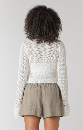 Person wearing a white textured sweater and beige shorts on a plain background