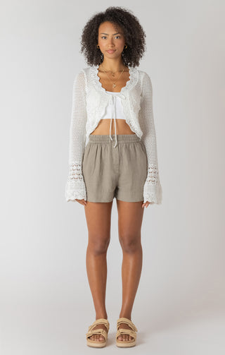 Woman wearing a white lace top and beige shorts on a plain background