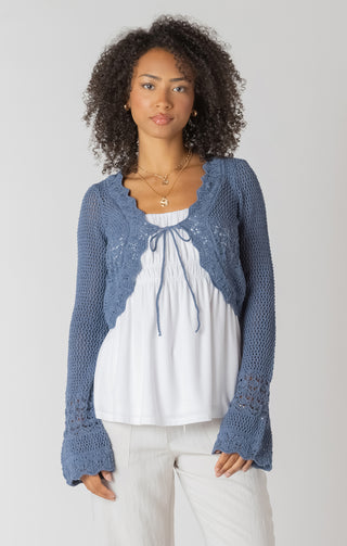 Woman wearing a blue knitted cardigan over a white blouse on a plain background
