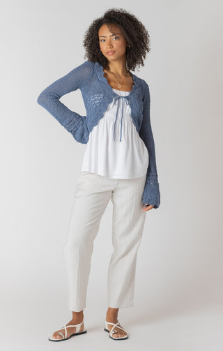 Woman wearing a blue cardigan, white top, and pants on a white background