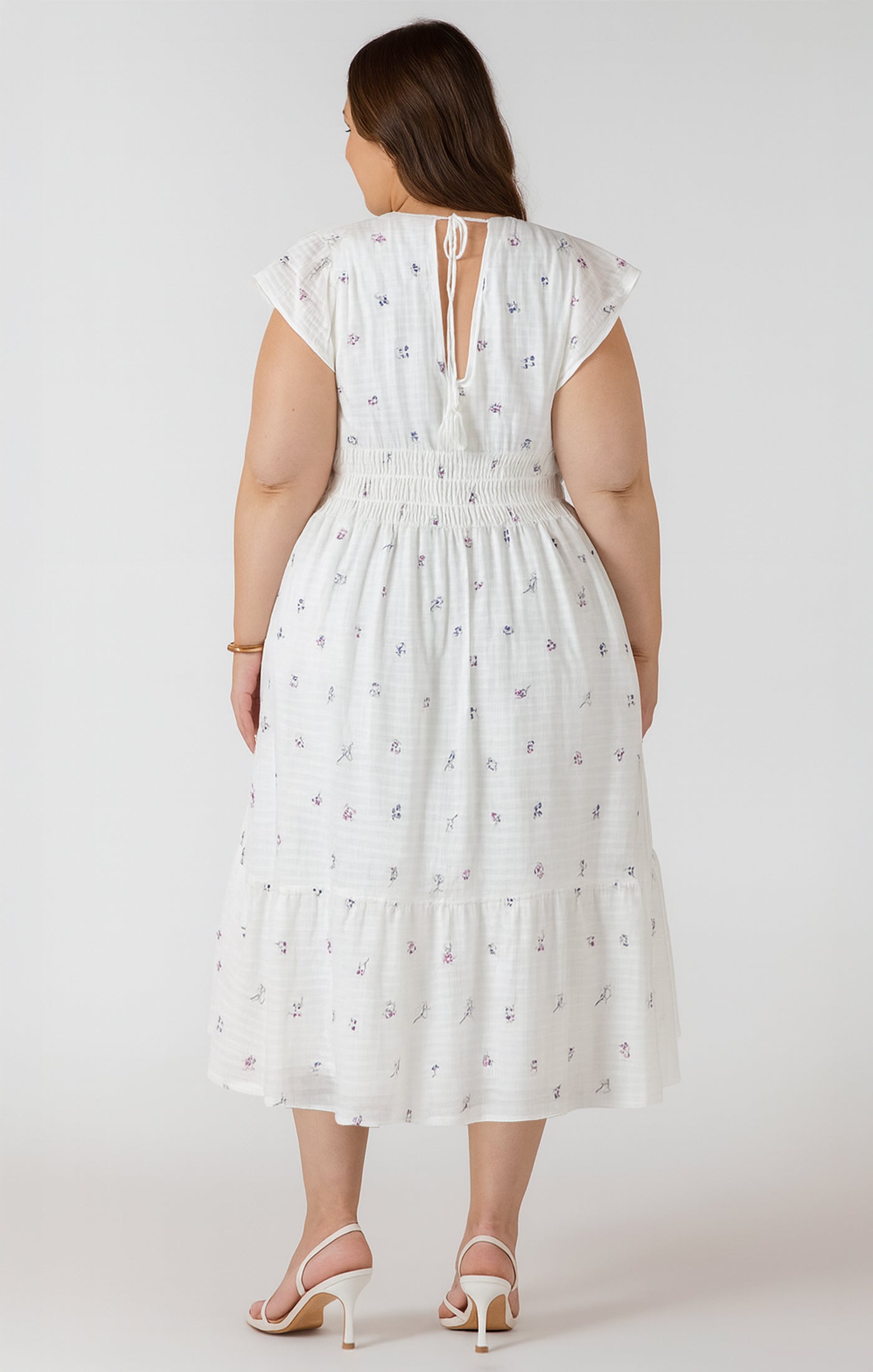 Woman wearing a white dress with floral patterns on a plain background