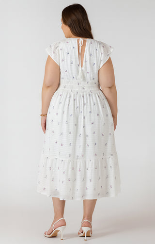 Woman wearing a white dress with floral patterns on a plain background