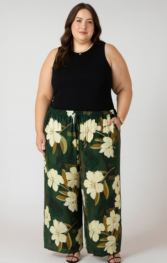 Woman wearing a black sleeveless top and green floral pants on a white background