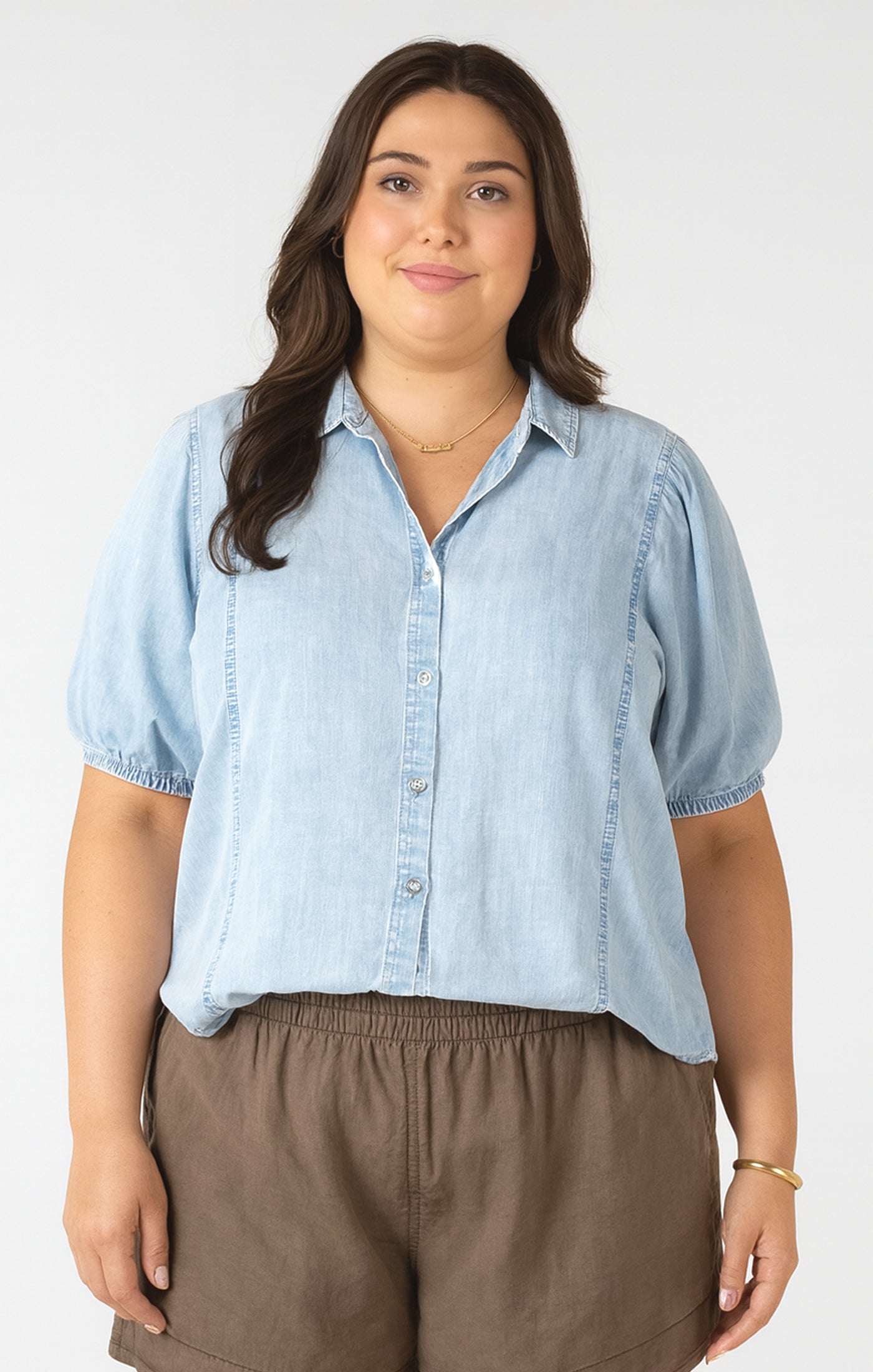 Woman wearing a light blue denim shirt and brown pants on a white background