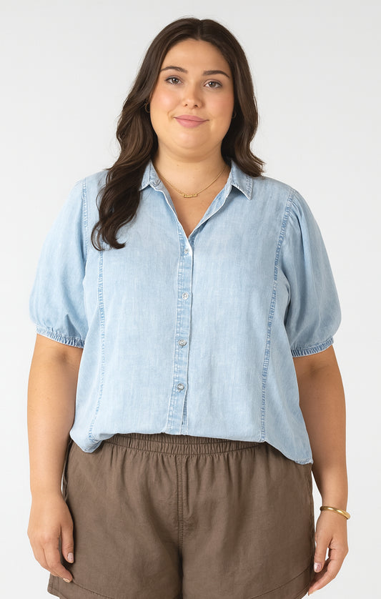 Woman wearing a light blue denim shirt and brown pants on a white background