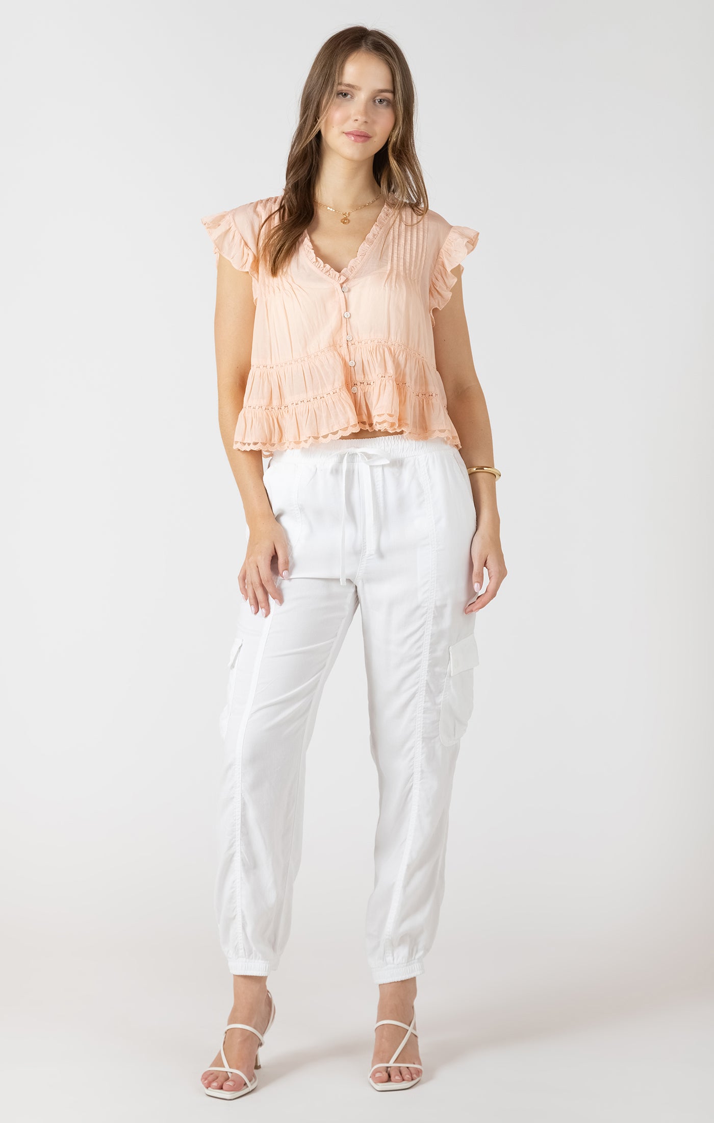 Woman wearing a peach top and white pants on a white background