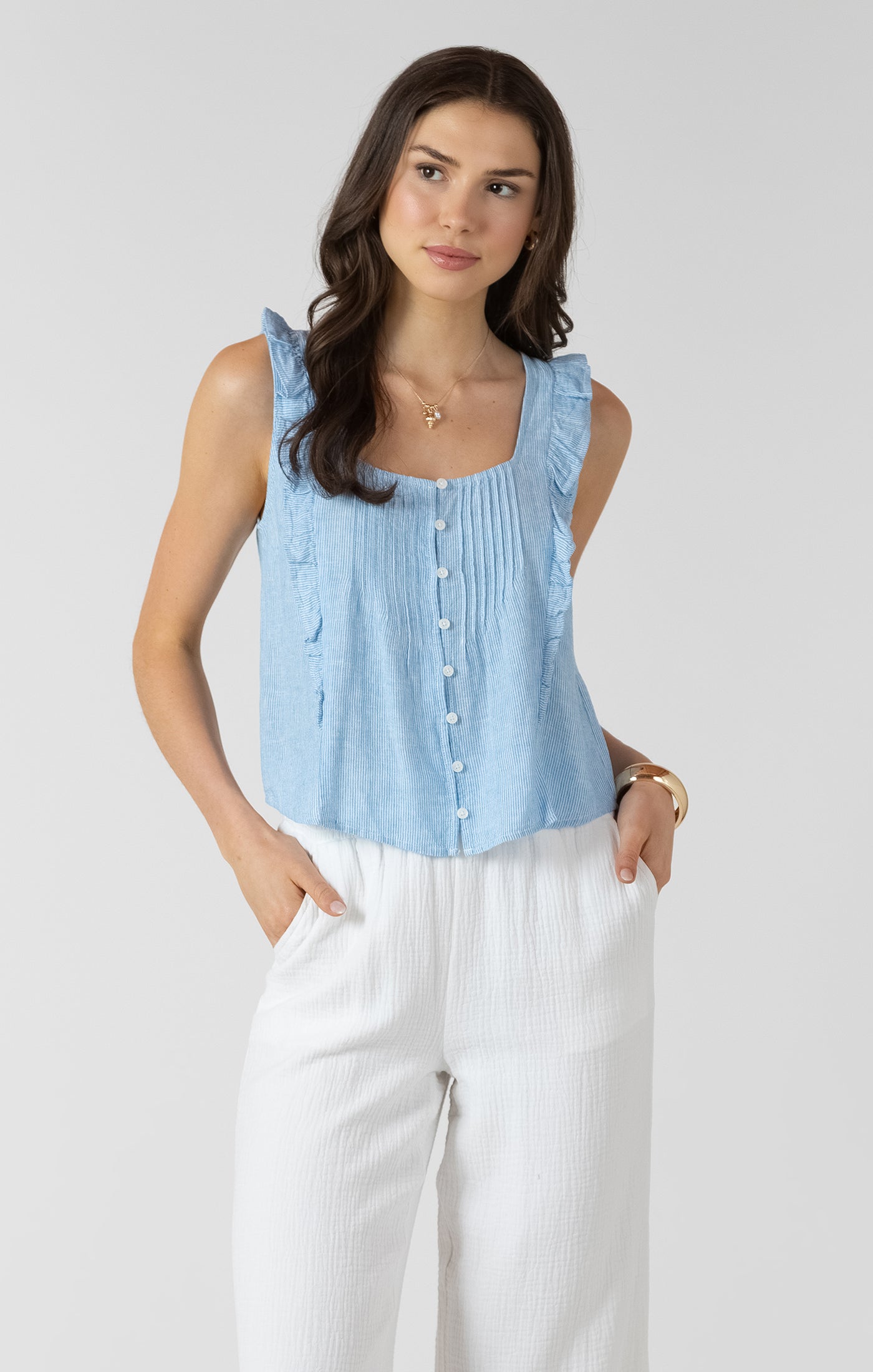 Woman wearing a light blue sleeveless top and white pants on a plain background
