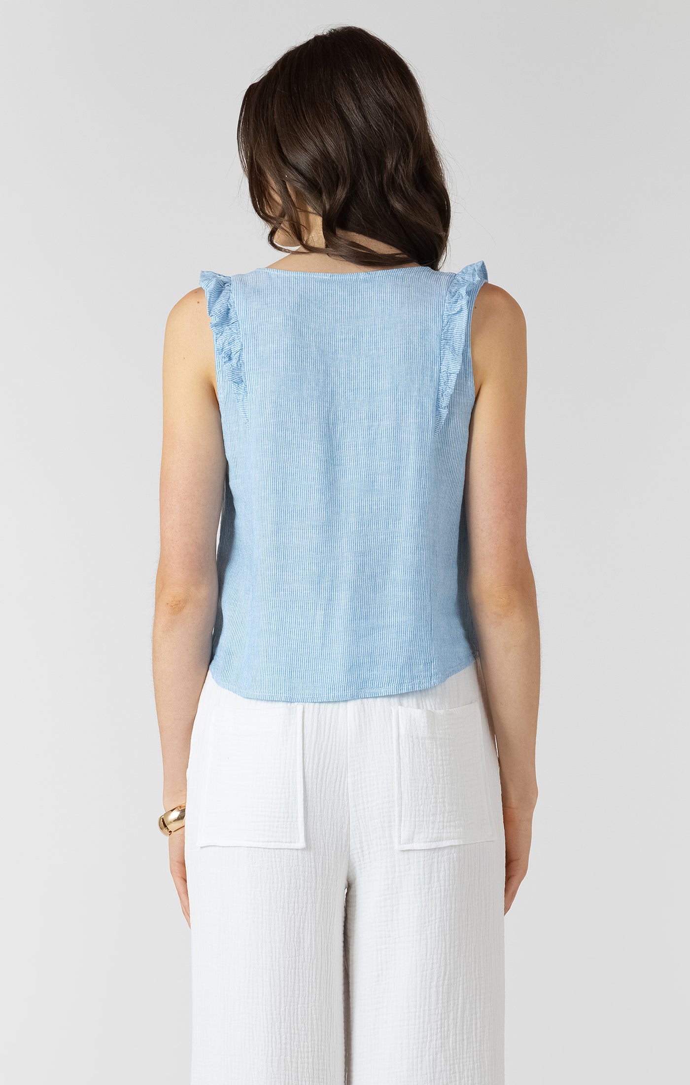 Woman wearing a light blue sleeveless top with ruffled shoulders on a white background