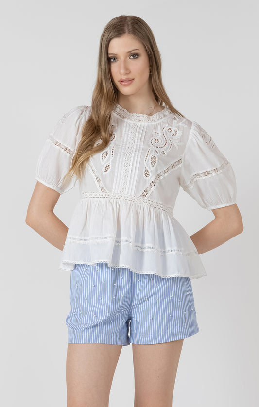 Woman wearing a white blouse with lace details and blue striped shorts on a white background