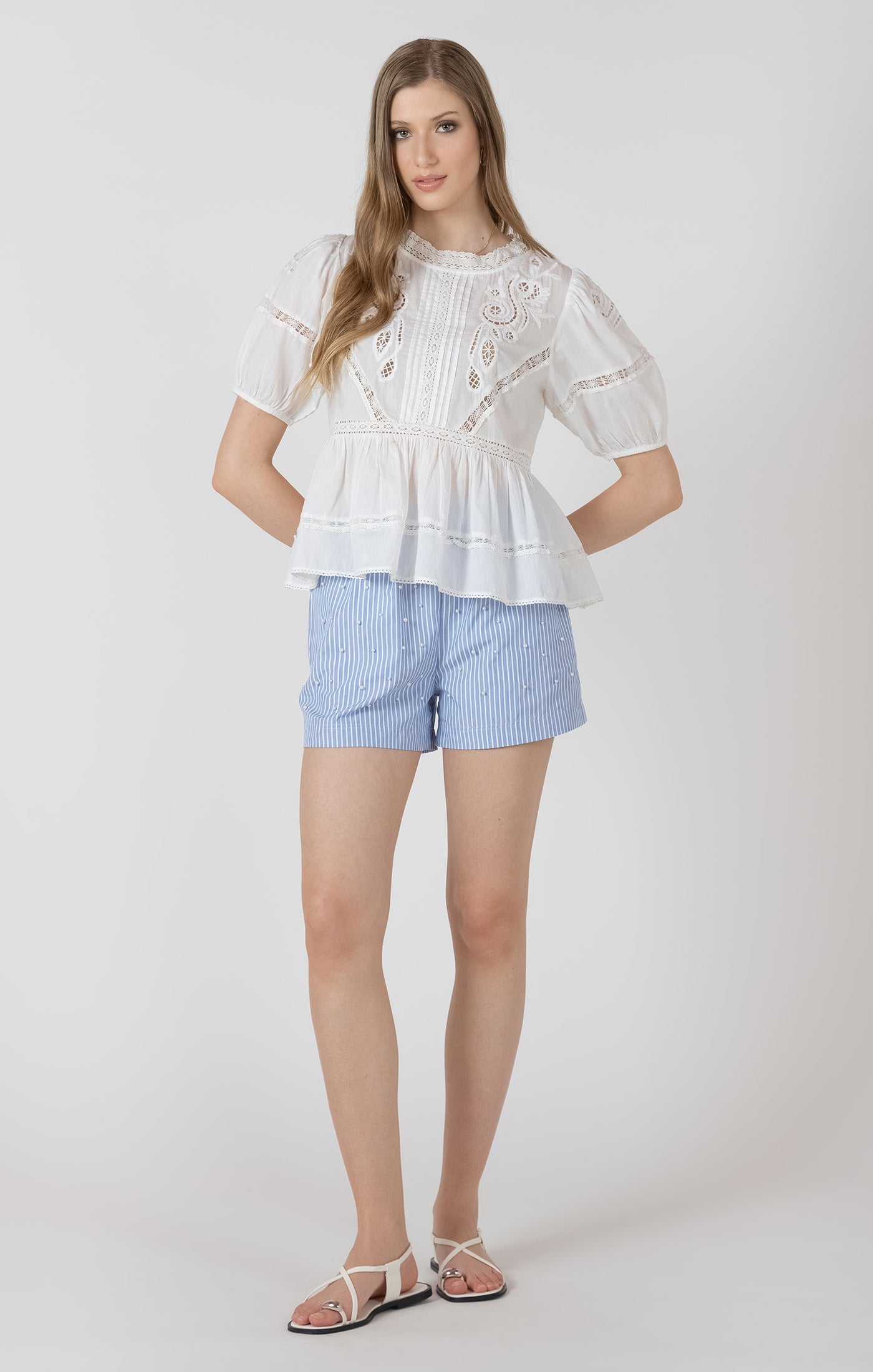 Woman wearing a white lace top and blue shorts on a white background
