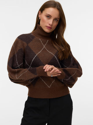 A woman wearing a brown argyle knit turtleneck sweater with balloon sleeves and black pants, photographed against a clean white studio background.