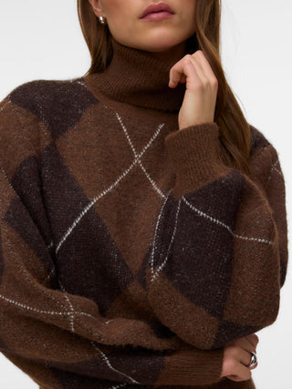A close-up of a woman wearing a brown and dark brown argyle knit turtleneck sweater with thin white intersecting lines, set against a plain white background.