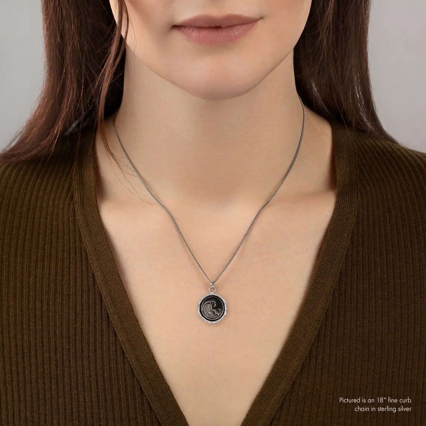 Person wearing a silver necklace with a pendant on a plain background