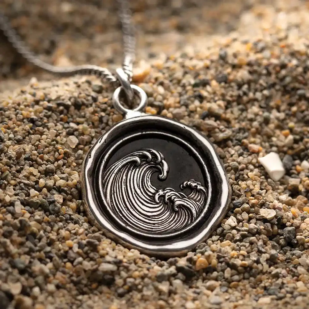 Silver pendant with wave design on a sandy background