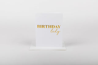 A white greeting card with 'BIRTHDAY lady' embossed in gold foil on the front, accompanied by a white envelope.