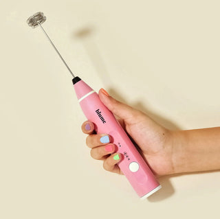 a hand holding a pink milk frother