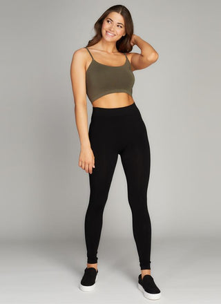 A woman standing, wearing black fleece-lined bamboo leggings with a green sports bra. 