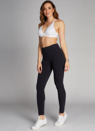 A woman standing, wearing black fleece-lined bamboo leggings with a white sports bra. 