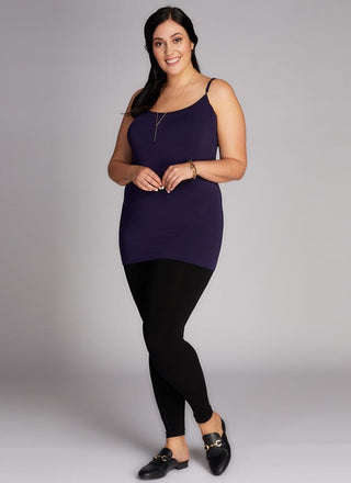 A woman wearing a navy tank top and black high-waisted leggings, standing against a grey background.
