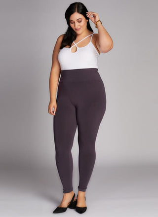 A woman wearing a white tank top and high-waisted leggings, standing against a grey background.