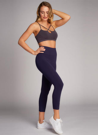 A woman is standing, wearing high-waisted  3/4 length leggings and a crop top. 