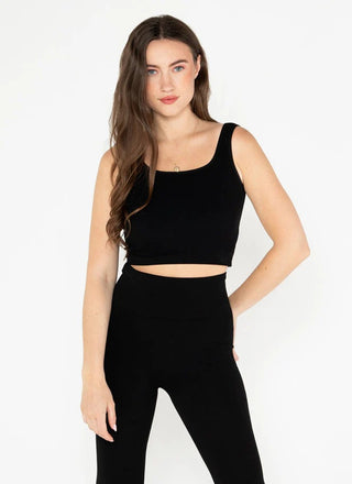 A woman wearing a square neck crop tank in a black color, with the tank displaying a ribbed texture.