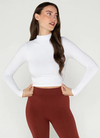Woman wearing a white long-sleeve top and red pants on a plain background