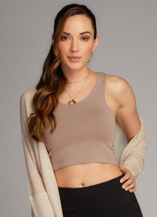 A woman wearing a taupe bamboo cropped tank top paired with blue jeans. 