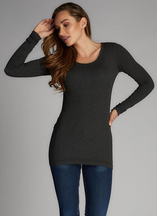 A woman wearing a long sleeve scoop neck top in grey, paired with blue jeans. 