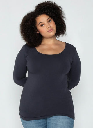 A woman wearing a dark grey long sleeve curvy scoop neck top paired with blue jeans.