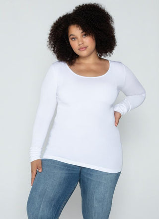 A woman wearing a white long sleeve curvy scoop neck top paired with blue jeans.