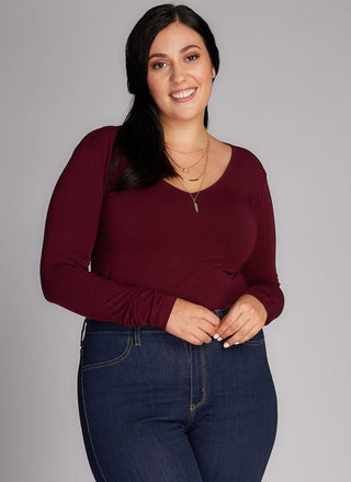 A woman wearing a red long sleeve v-neck top paired with blue jeans.