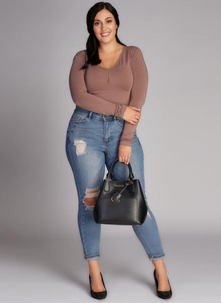 A woman wearing a brown long sleeve v-neck top paired with blue ripped jeans.
