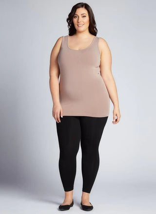 Woman wearing a beige tank top and black leggings on a plain background