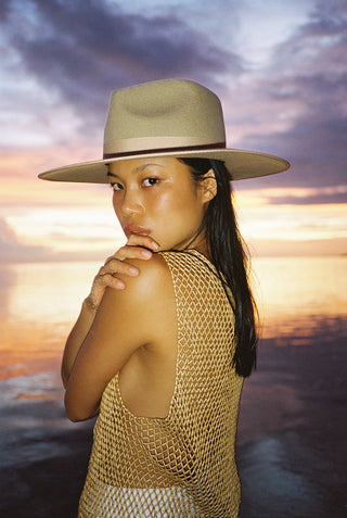 A woman wearing a beige-colored wool fedora hat with a tonal gross grain ribbon trim.