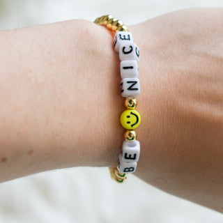Bracelet with letter beads spelling 'BE NICE' on a wrist against a white background