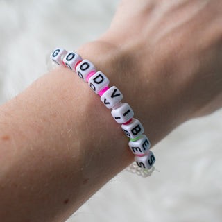 Bracelet with 'GOOD VIBES' beads on a wrist against a neutral background