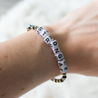 Bracelet with 'STRONGER' beads on a wrist against a neutral background