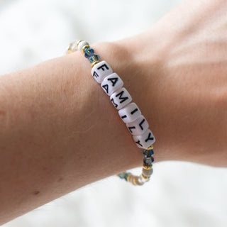 Bracelet with letter beads spelling 'FAMILY' on a wrist against a white background