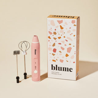 Pink milk frother with 'blume' branding next to its packaging on a beige background