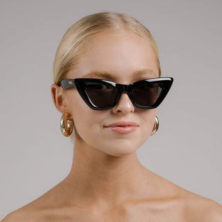 Woman wearing black cat-eye sunglasses with a plain background