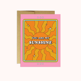 Card with orange and yellow sunshine drawing with text stating You Are My Sunshine, on a pink background. 