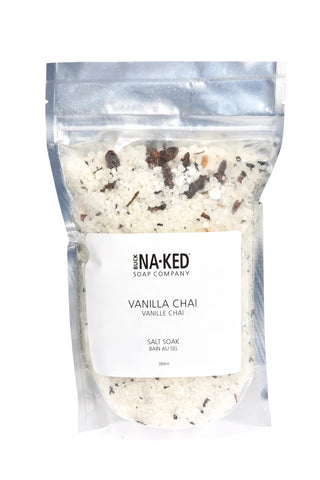 A clear plastic package containing white bath salts with small pieces of brown spices mixed in, labeled 'VANILLA CHAI' in bold letters.