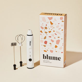 White milk frother with 'blume' branding next to its packaging on a beige background