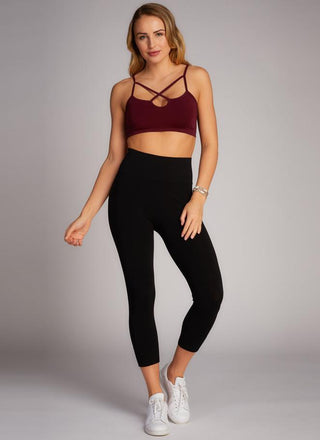 A woman is standing, wearing high-waisted black 3/4 length leggings and a red crop top. 
