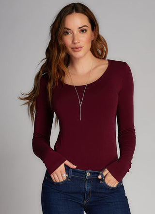 A woman wearing a long sleeve scoop neck top in red, paired with blue jeans. 