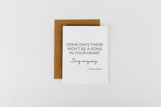 A greeting card with a quote printed on it, accompanied by a brown envelope. The card is placed against a white background.