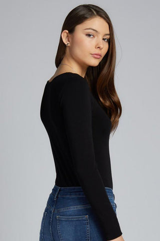 A woman wearing a long sleeve scoop neck top in black, paired with blue jeans. 